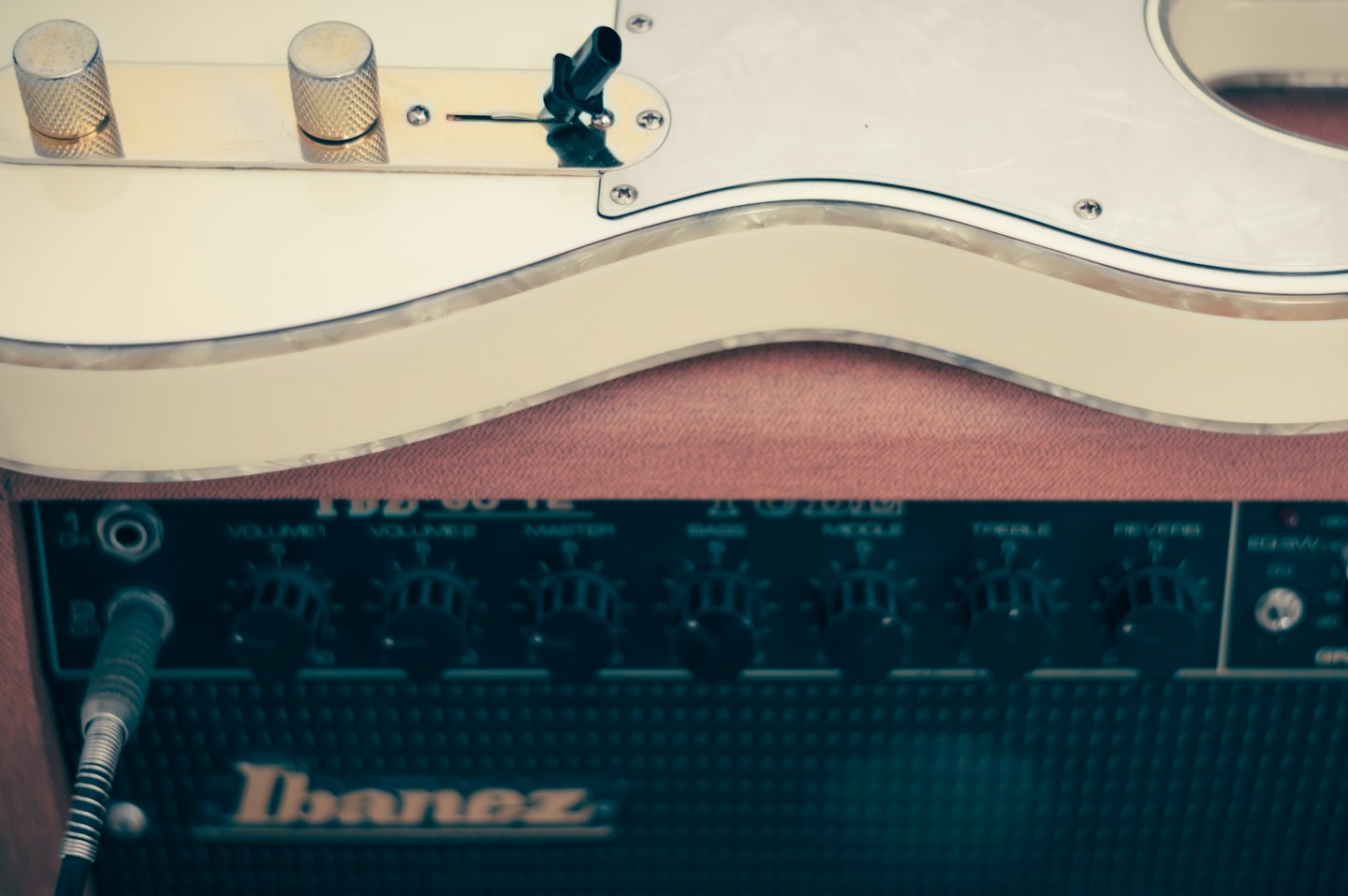 Biela elektrická gitara spočíva na hnedý textúrovaný zosilňovač.